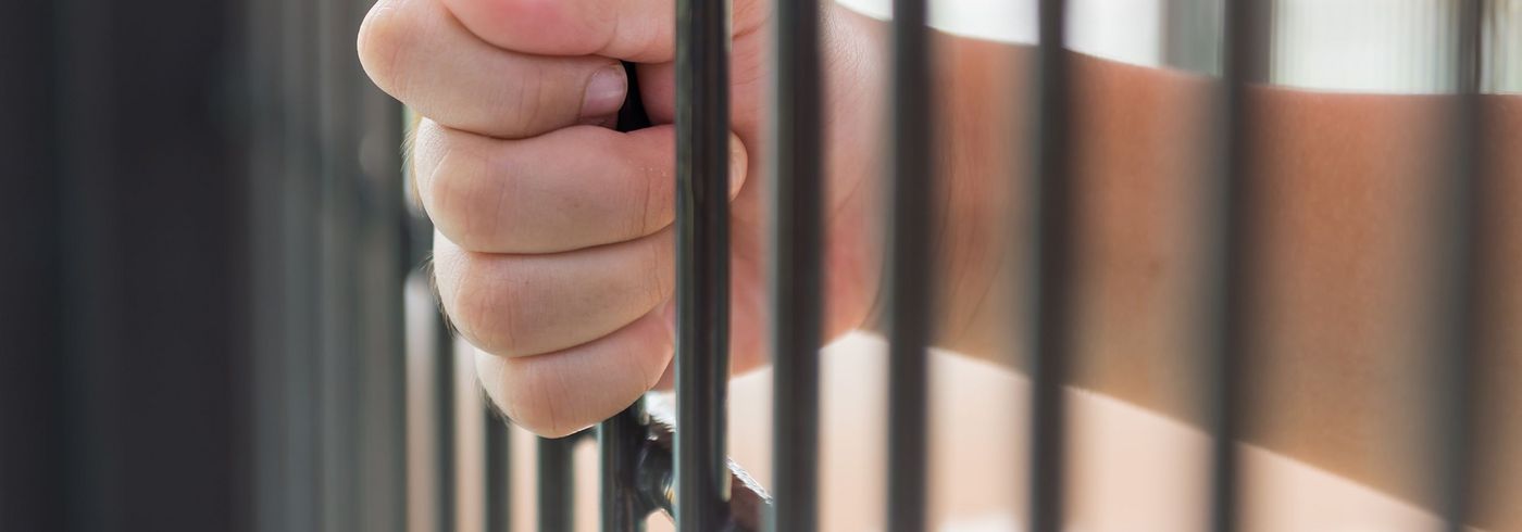 Hand, welche Gefängnis-Gitterstäbe umfasst
